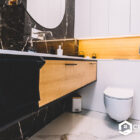Luxury bathroom with black marble walls, wooden vanity, and a modern toilet