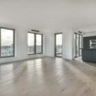 For this image, the alt text could be "Modern open-concept living space with hardwood flooring and large windows, adjacent to a kitchen